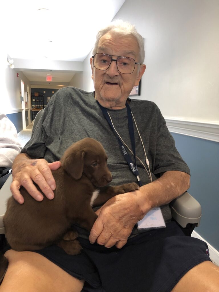 Elderly man holding a puppy in a hallway.