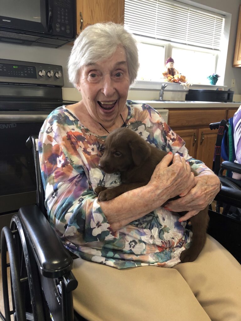 A resident joyfully holding a puppy in a kitchen.