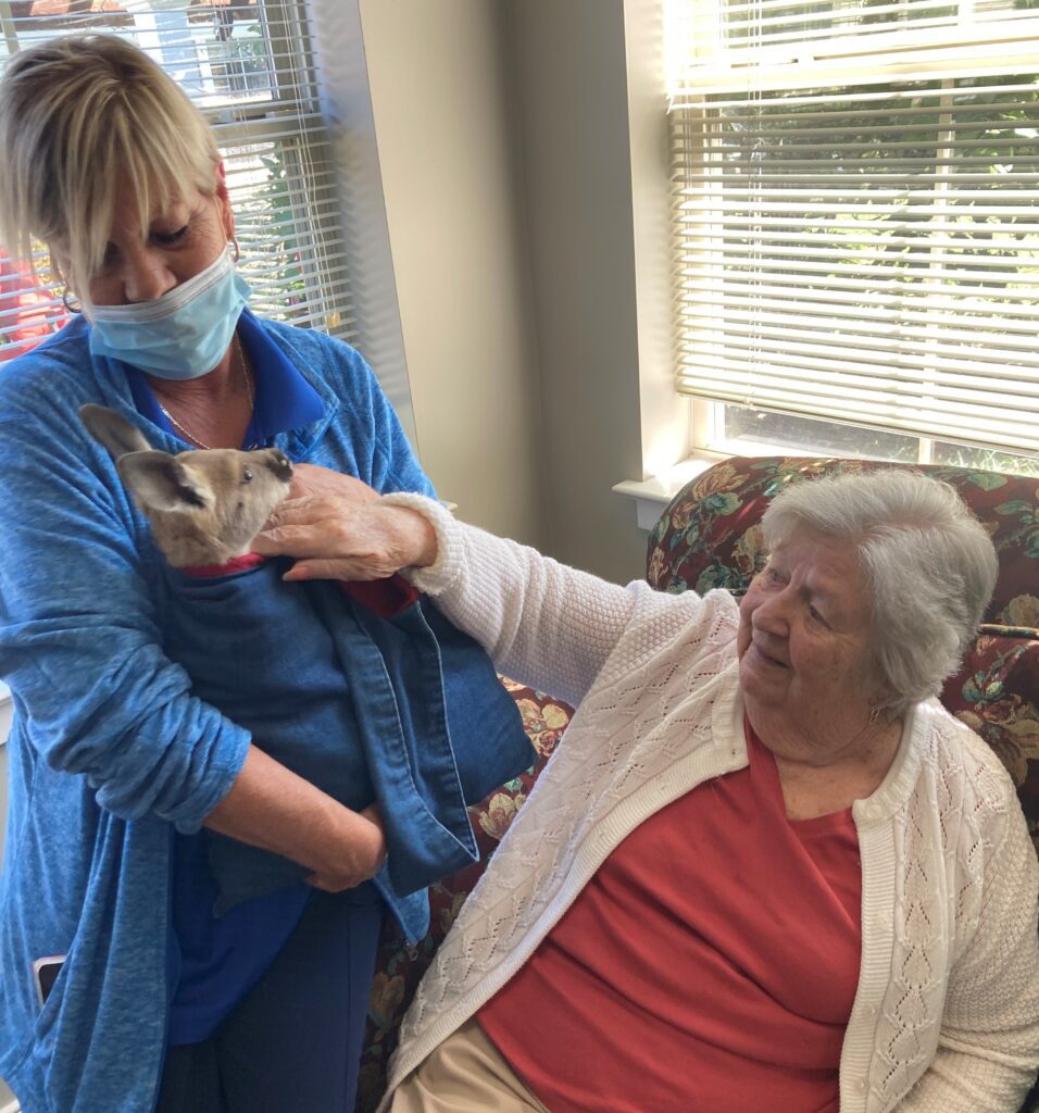 Resident interacting with staff and a small dog indoors.