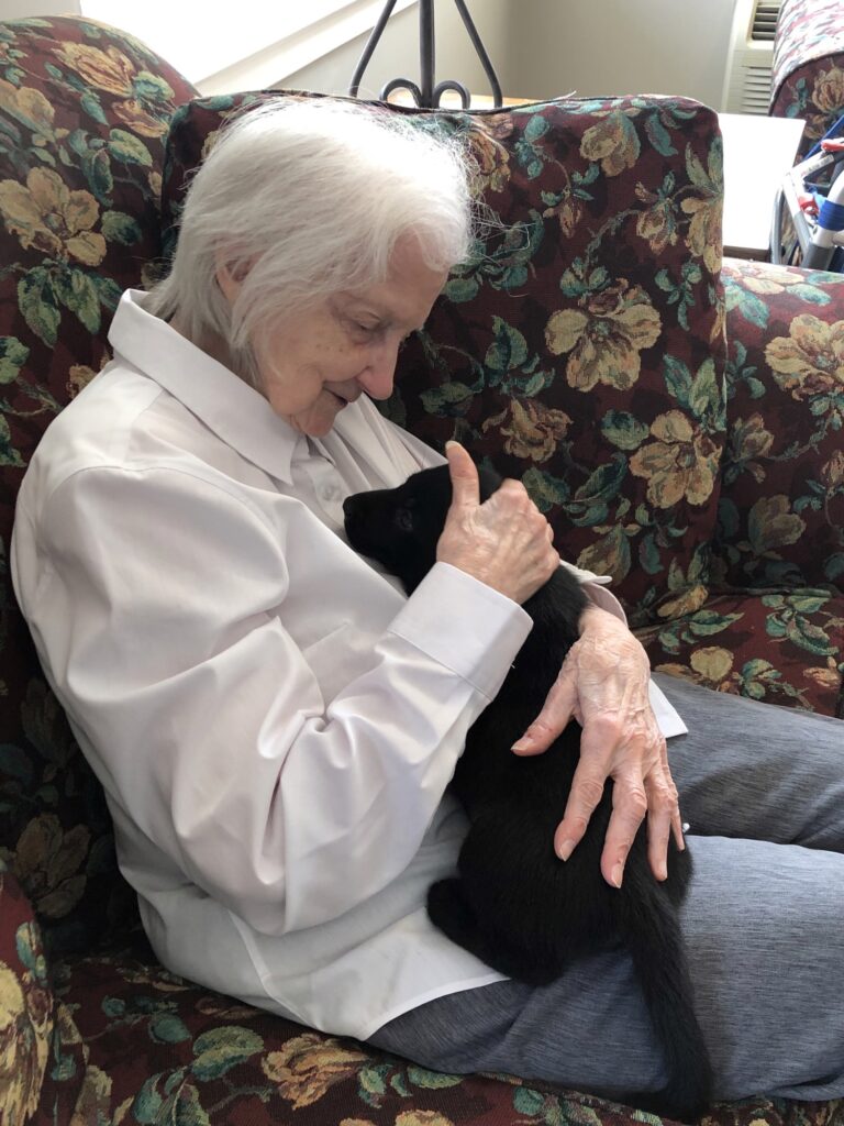 Senior resident cuddling a black cat on floral couch.