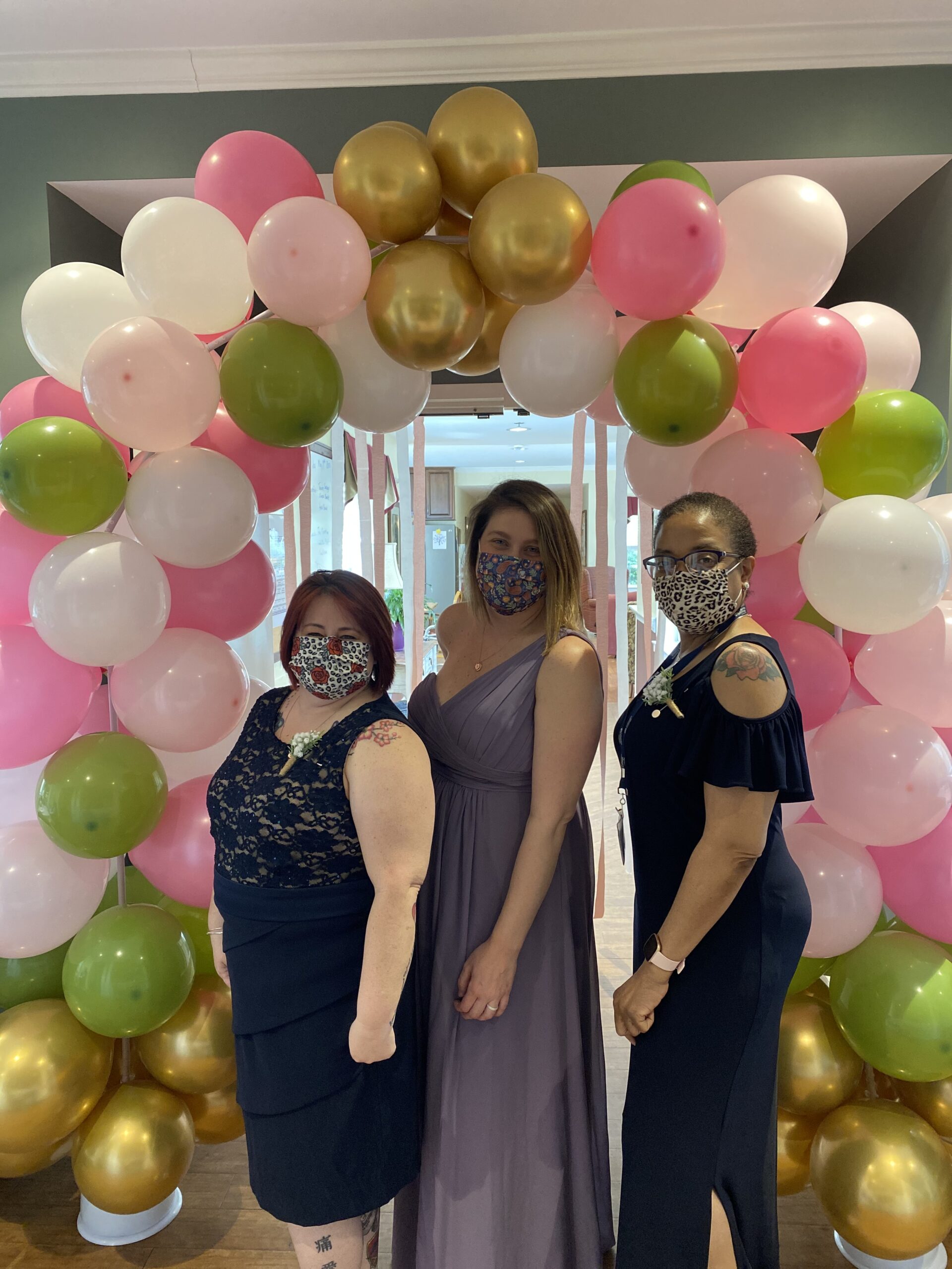 Three staff members posing in front of a balloon arch.