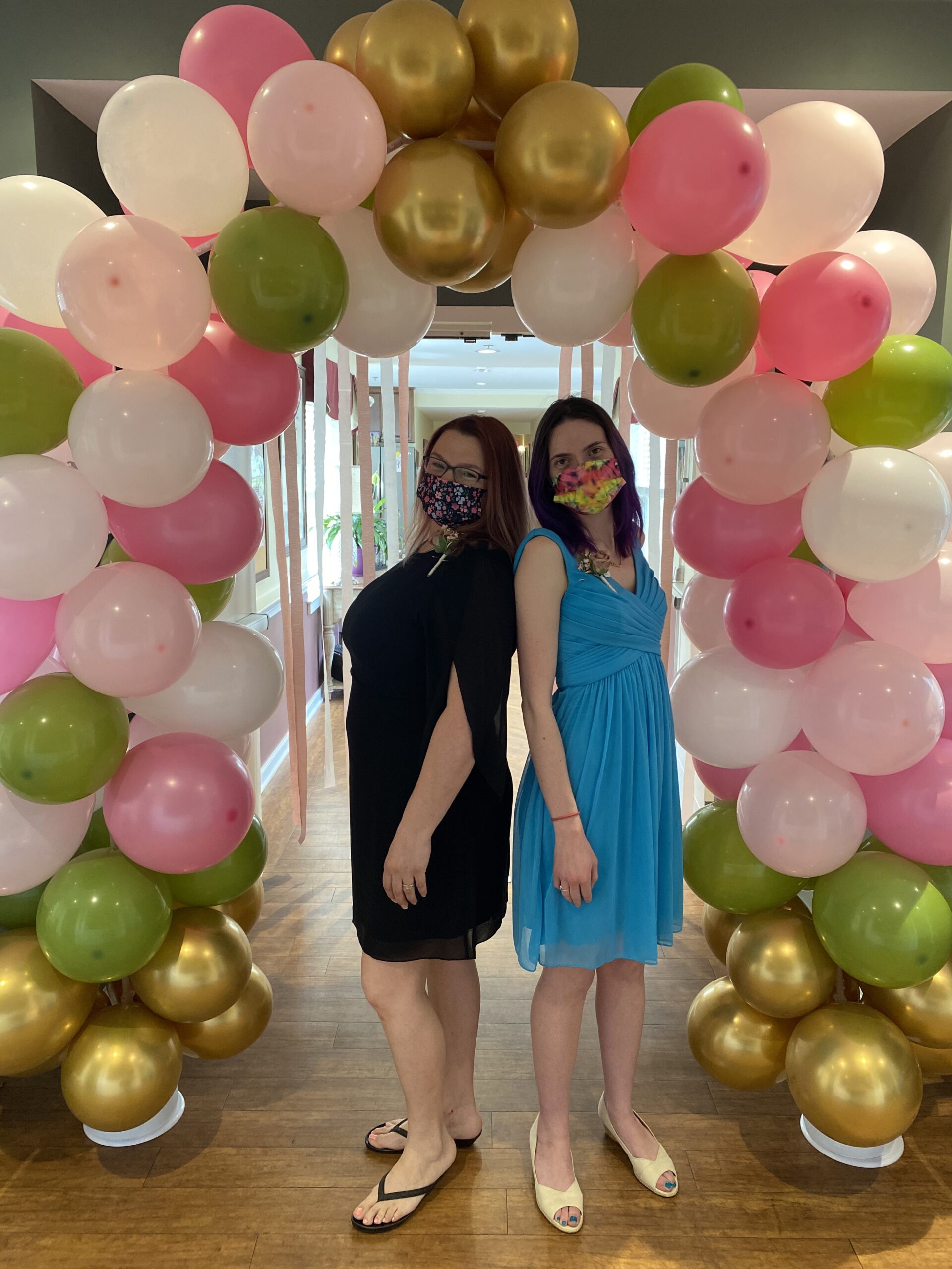 Two women posing in front of a colorful balloon arch.
