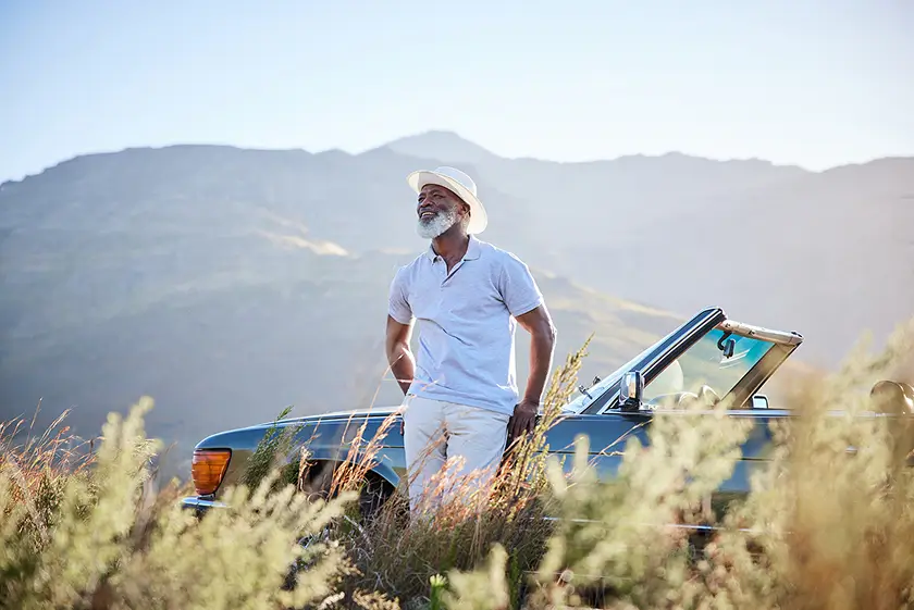 A senior man standing next to a convertible car in a field
