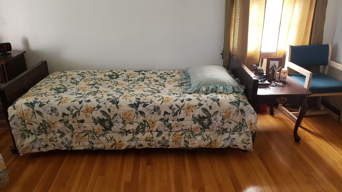 A resident room with a floral patterned bedspread and chair.